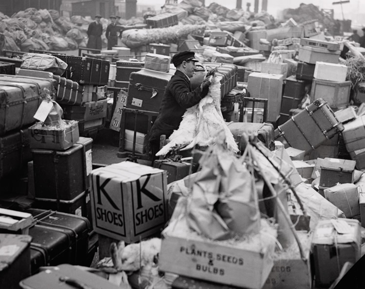 A station luggage handler surrounded by Christmas parcels and suitcases at Waterloo, December 1936. (Img ref: 10308463).