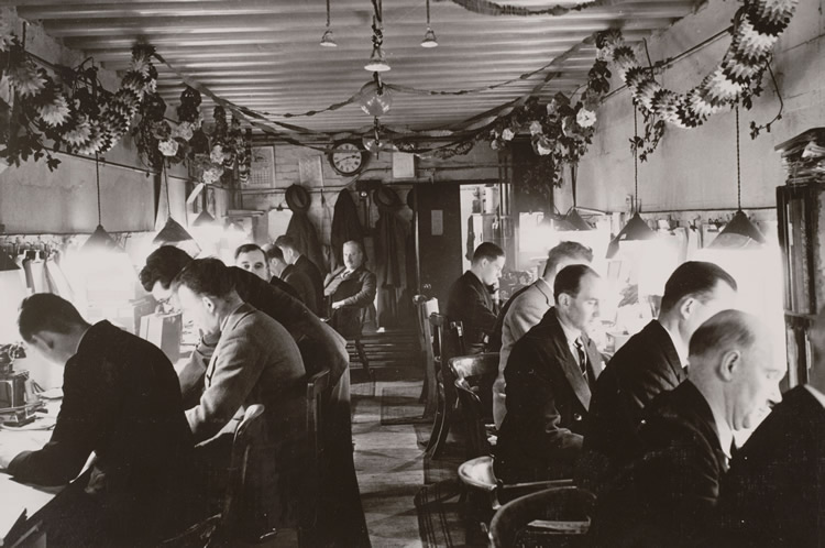 Railway workers in a control room on the Southern Railway, Christmas 1940. These workers booked freight onto certain trains, and recorded the items needed transporting to their destination when they were unloaded from the train. Control room workers also dealt with problems along the track, such as with signals or points. This photograph was taken during the Second World War and, as an official photograph, needed to be passed by a censor. (Img ref: 10451590)