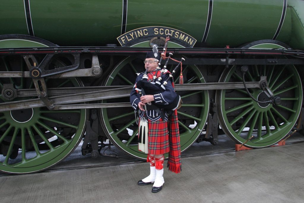 A bagpipe player stands in front of the locomotive Flying Scotsman.