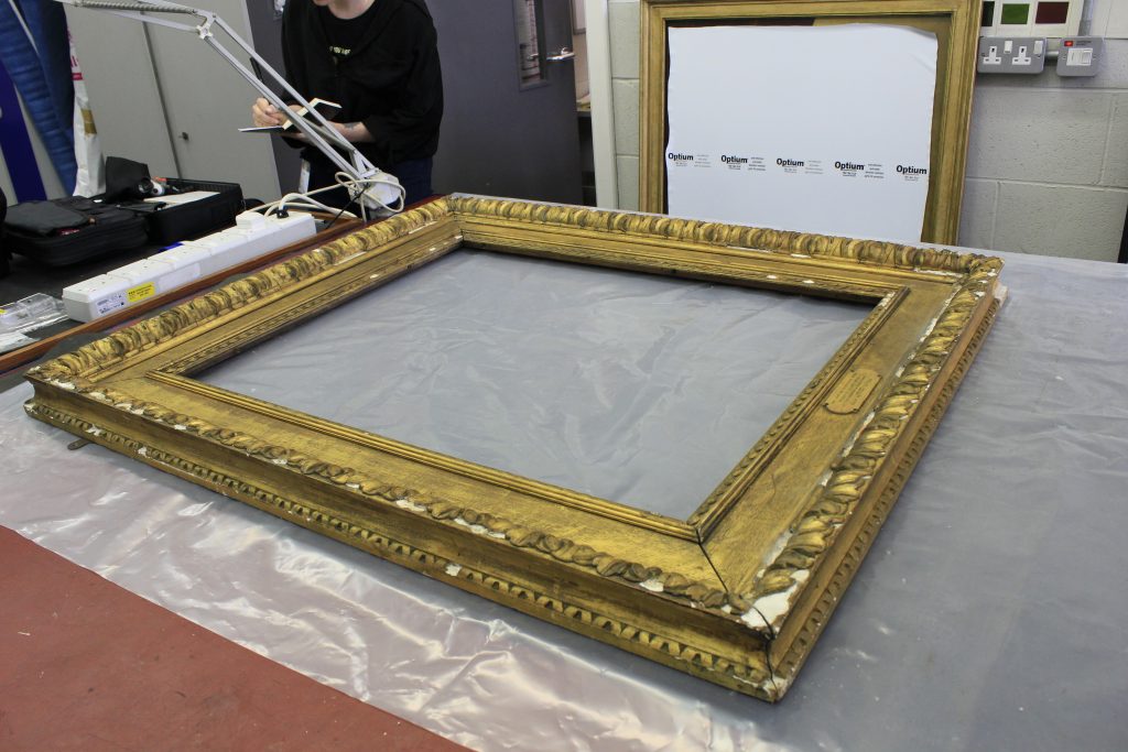 A damaged gold picture frame on the conservation workshop bench