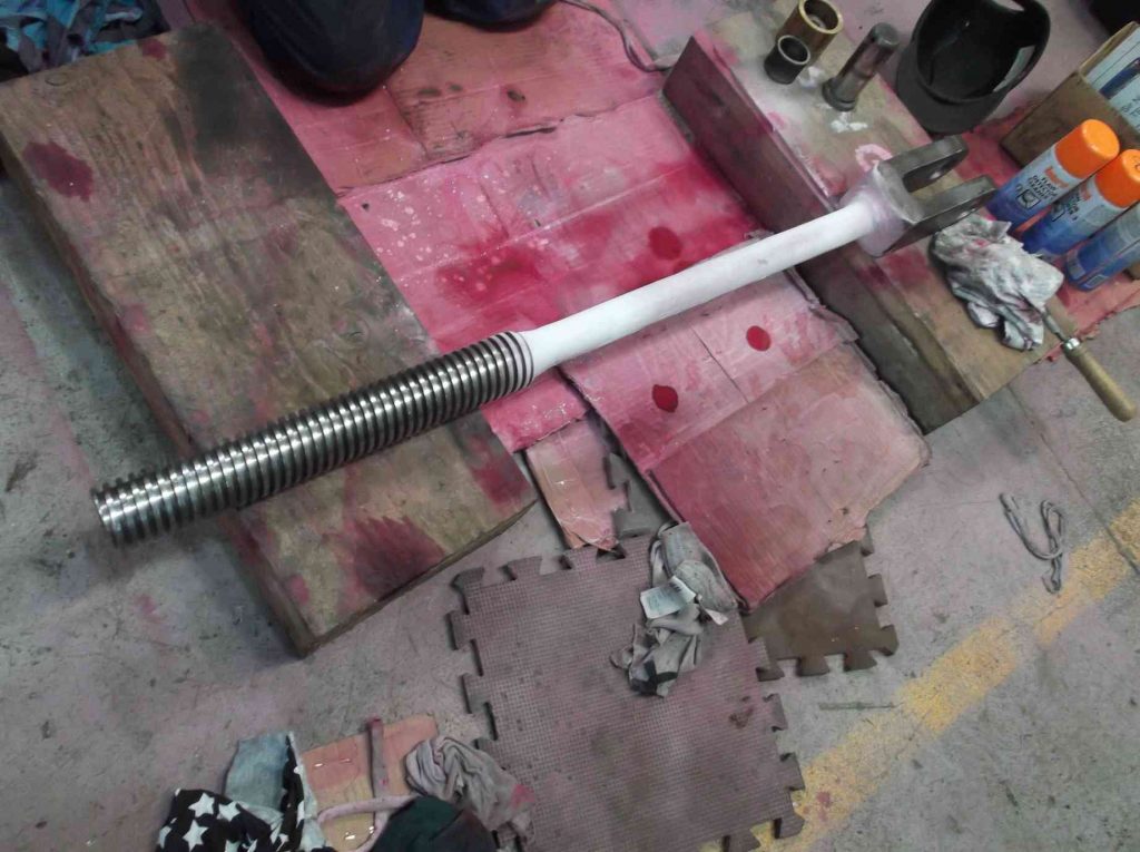 Reverser screw on the workshop floor, being examined for defects.
