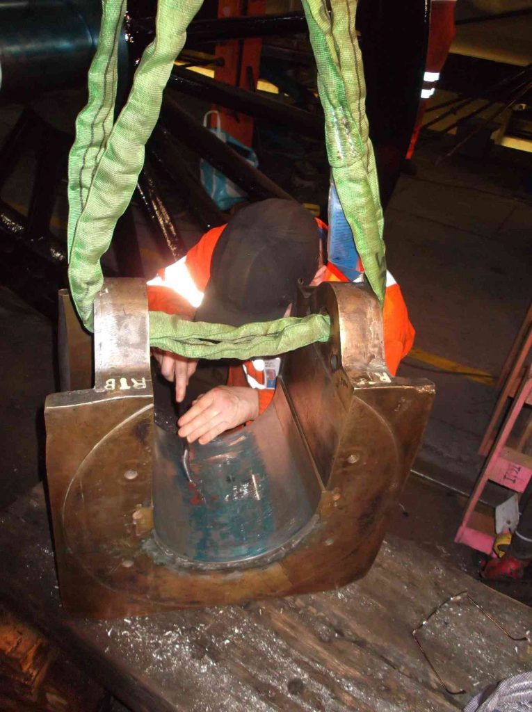 A man in orange hi-vis jacket scrapes a locomotive axlebox