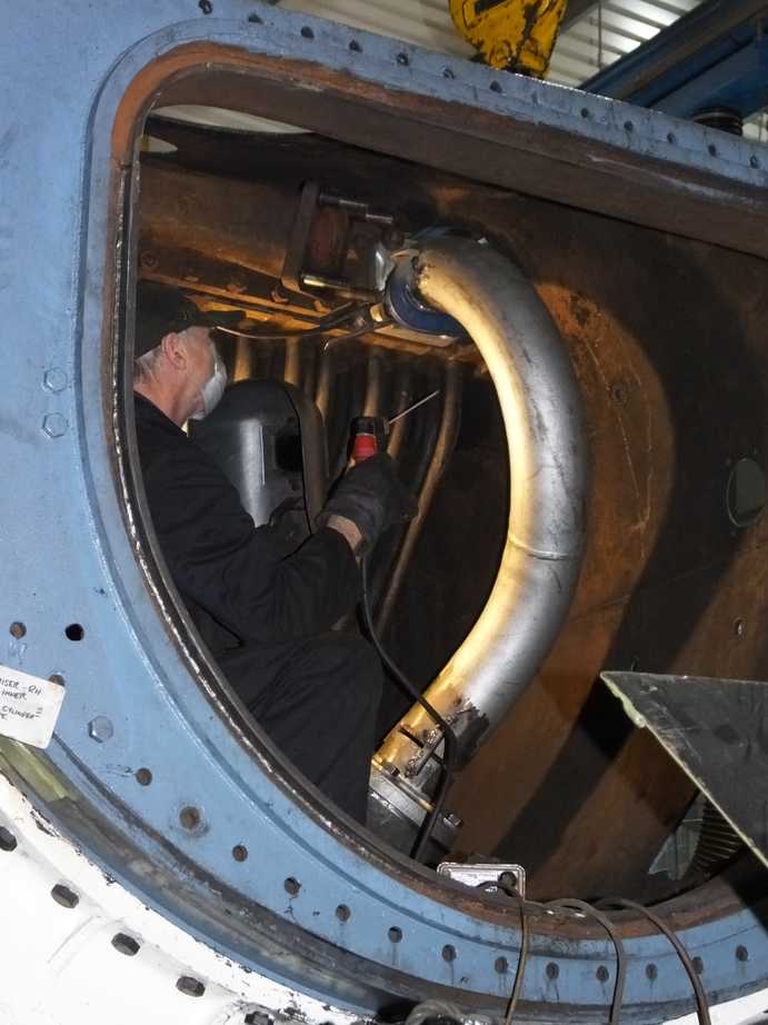 A person in overalls sits inside the locomotive holding a hand tool