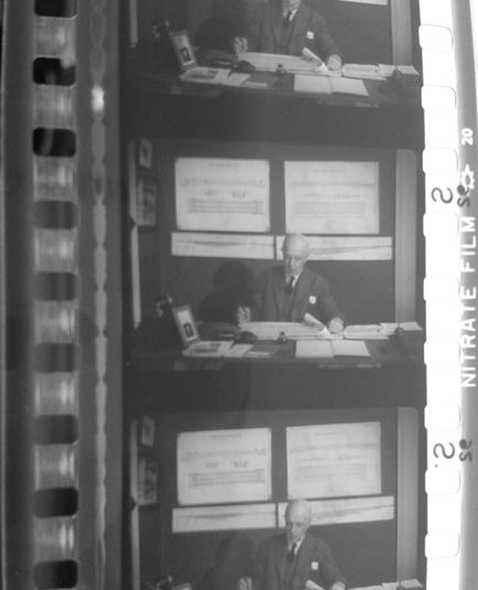 This is a picture of a 35 mm safety print (acetate base) of the black and white sound film “The Kearney Monorail” (another film about the Kearney Railway). On top of the picture, below the perforation you can see the optical sound track, then the frames, and on the edge below the perforation in the bottom of the picture the printed “Nitrate film” and blast symbol in white on a grey back ground. These were printed on this safety film from a previous nitrate negative element.