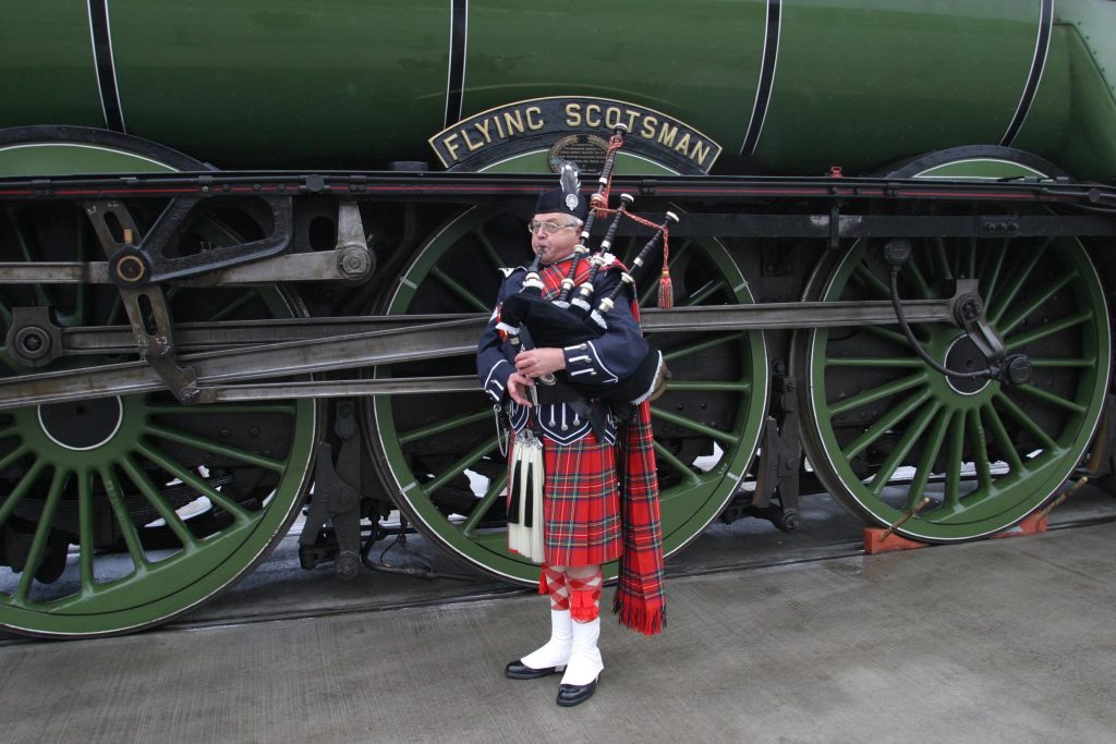 A bagpipe player stands in front of the locomotive Flying Scotsman.