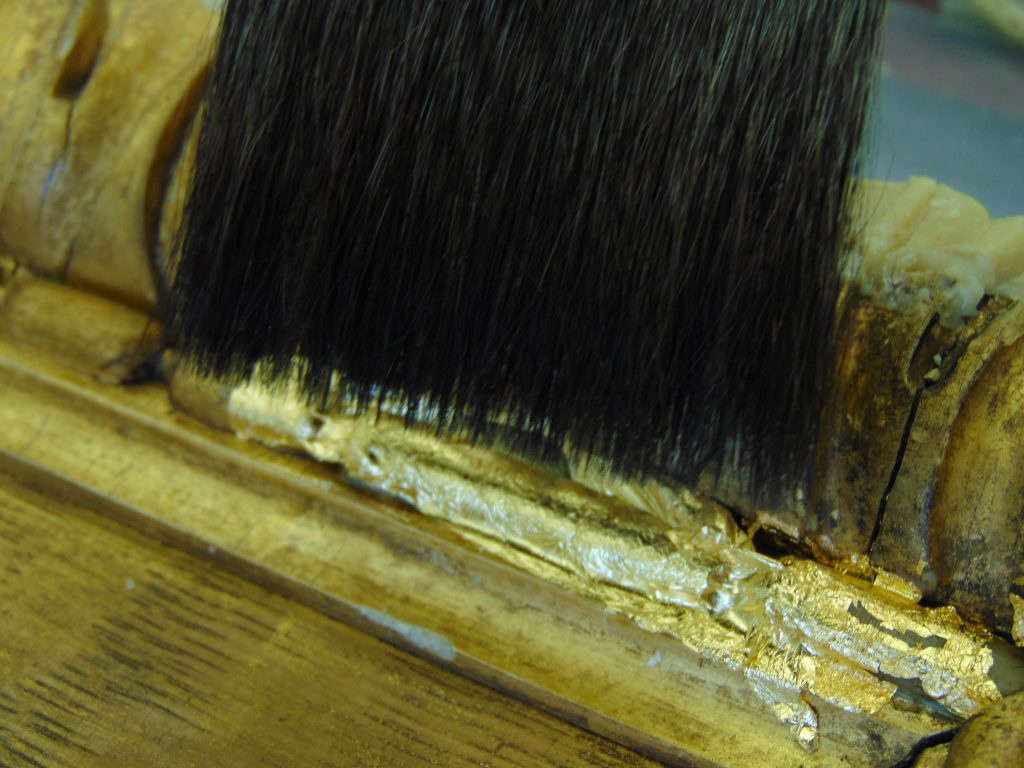 Gold leaf being applied to a picture frame using a flat squirrel hair brush